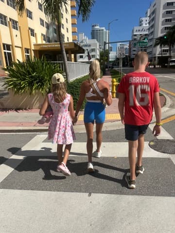 A family of four walking together on a sidewalk, seen from behind