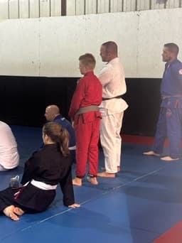 A boy in a red gi kneeling on the mats